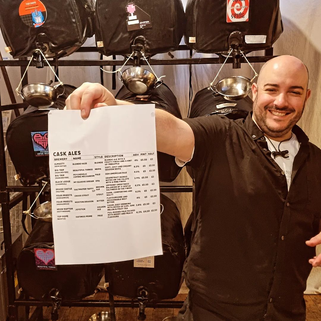 person holding menu of beers in front of beer casks